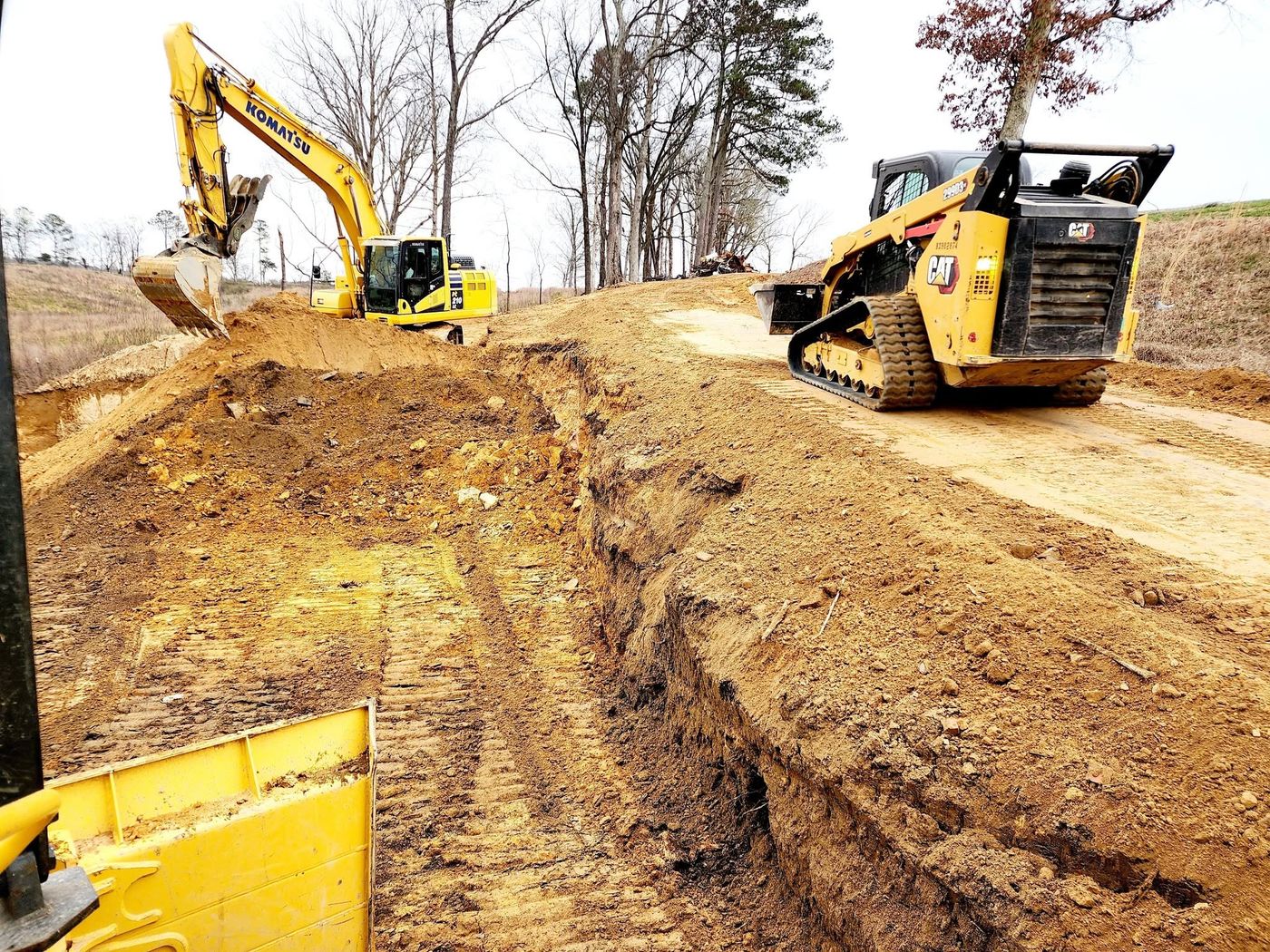 Excavator and skid steer cutting a bank on a hillside