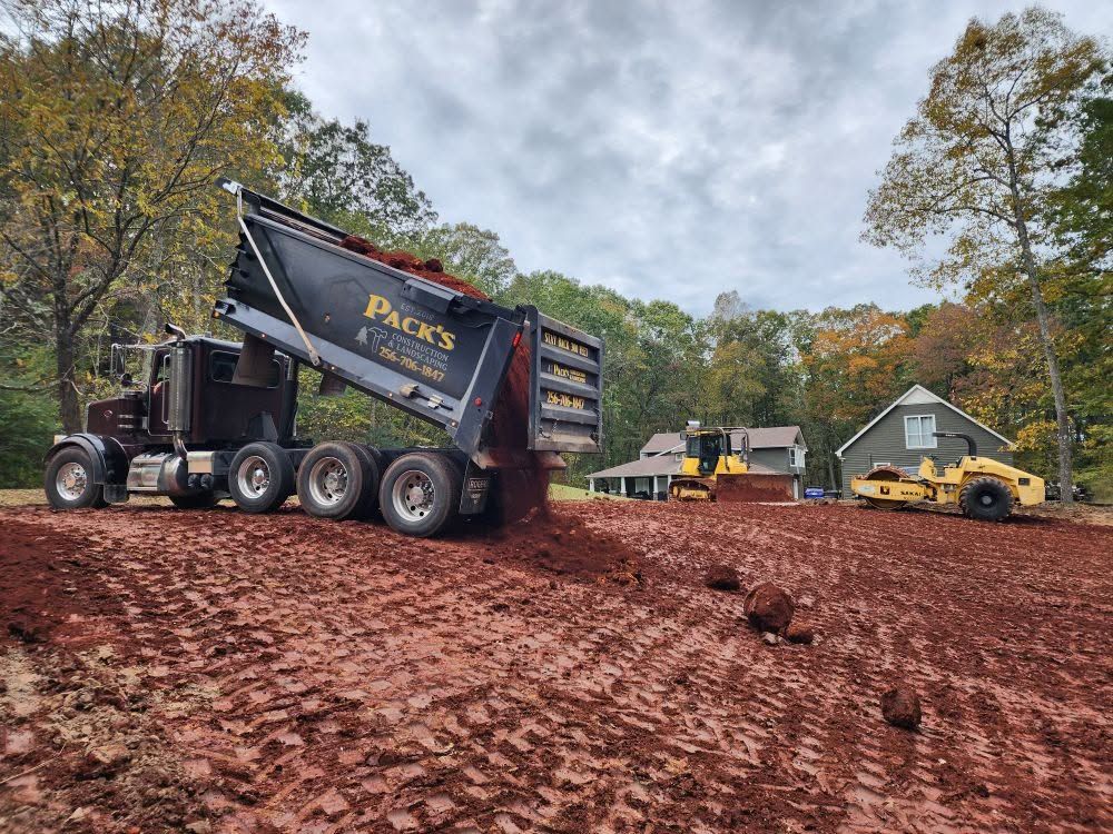Pack's dump truck tailgating fill dirt across a pad